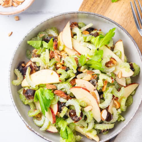 celery apple salad with dates in a grey bowl with a wooden board.