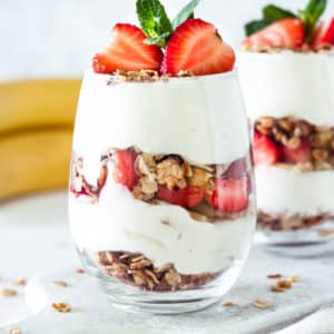 Granola yogurt breakfast parfait in a glass cup topped with fresh strawberries and mint.