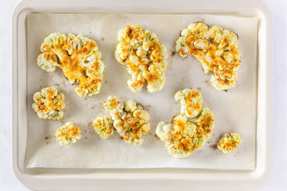 spices atop roasted cauliflower with olive oil on a baking tray with parchment paper.