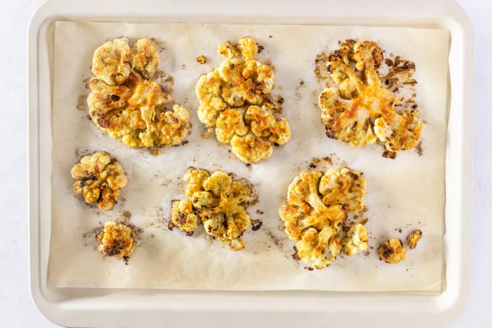 roasted cauliflower slices on parchment paper and a baking tray.