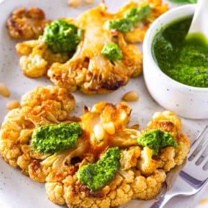 a silver fork on a grey plate with roasted cauliflower steak and pesto on it.