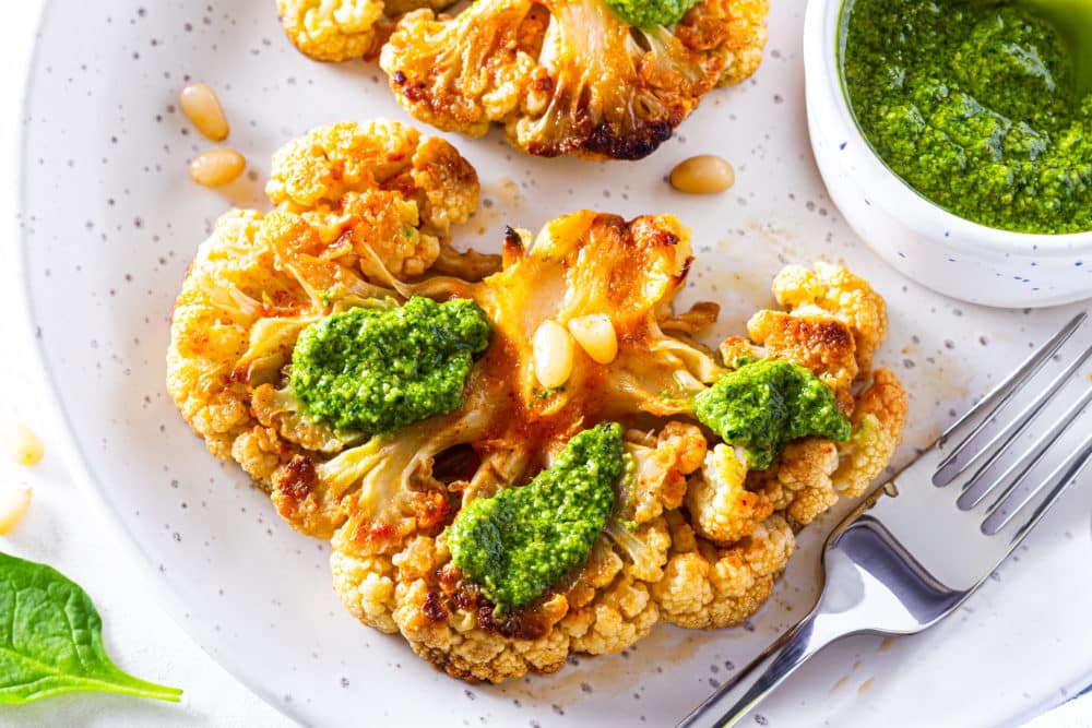 white-plate-with-silver-fork-and-roasted-cauliflower-steak-with-pesto-and-pine-nuts-with-a-small-white-bowl-of-pesto