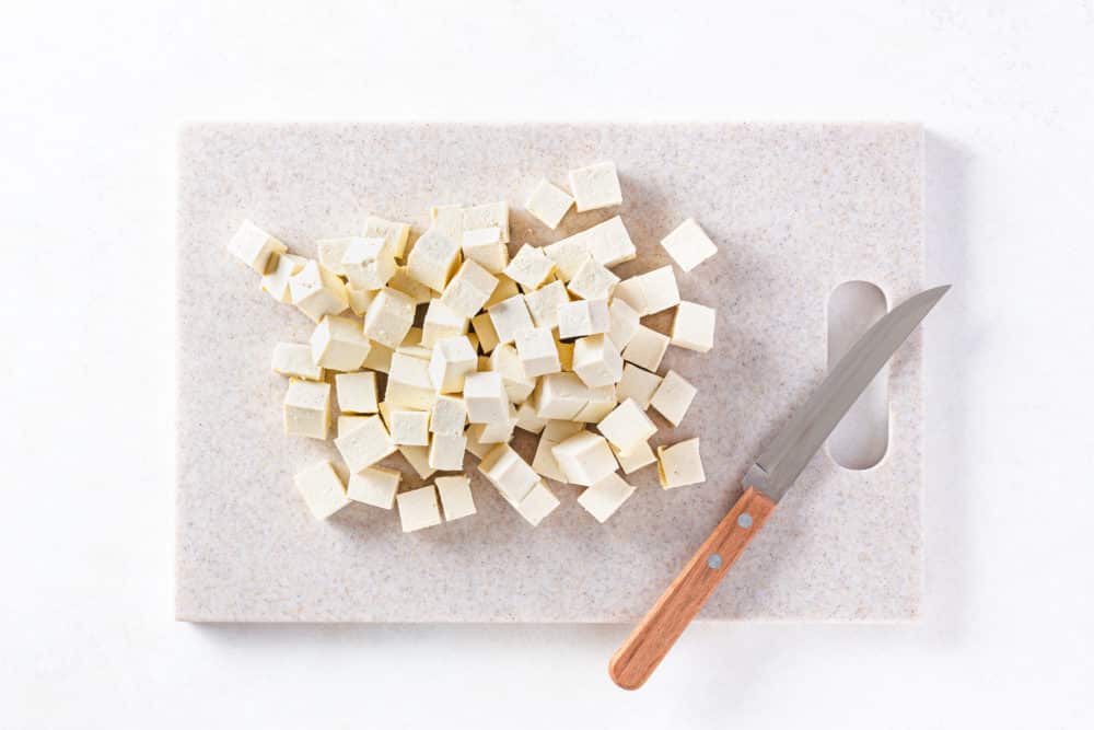 chopped tofu on a cutting board with a knife.