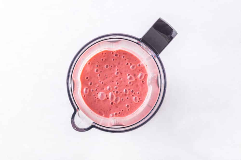 a blender with a pink blended strawberry smoothie inside.