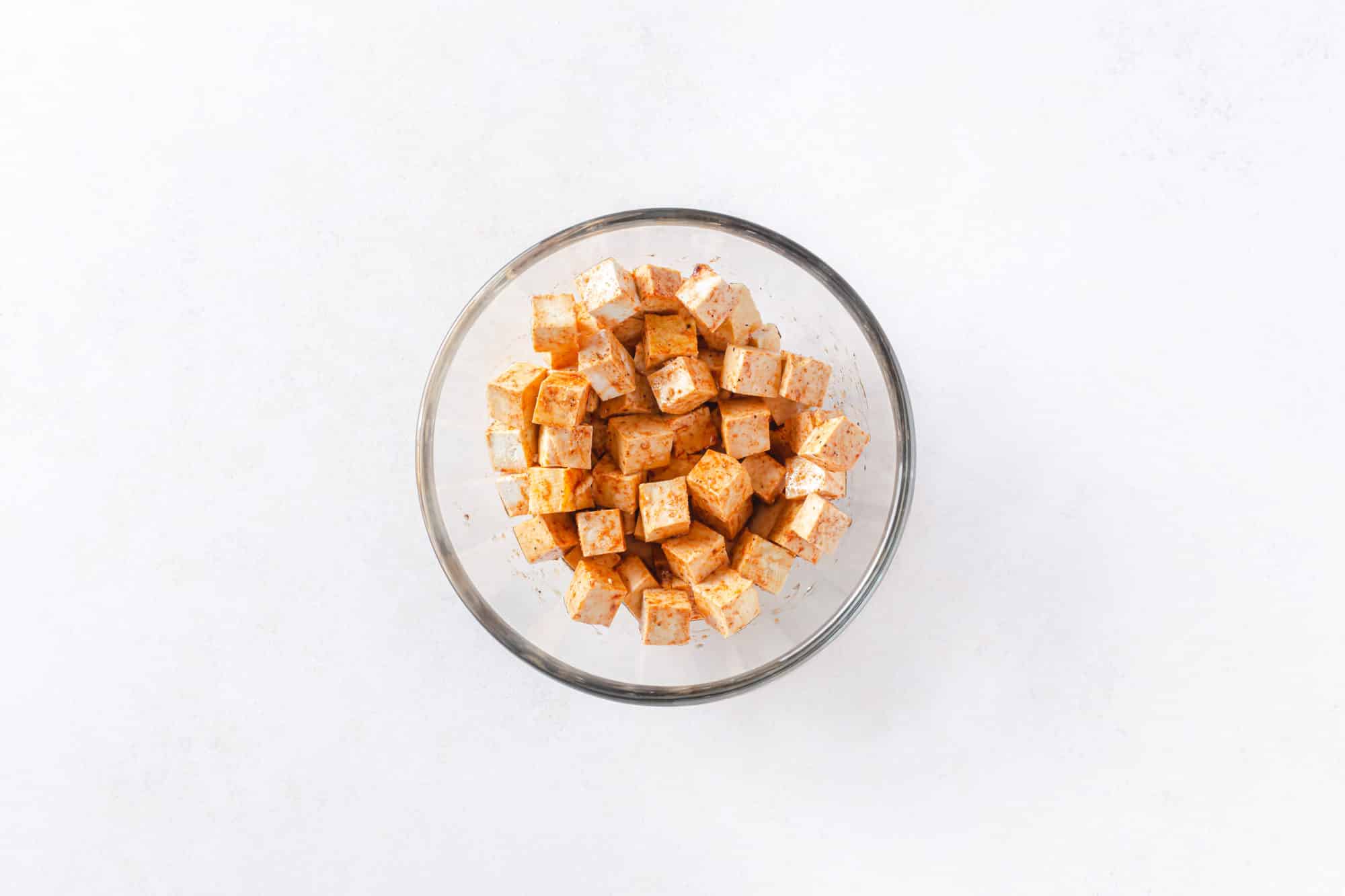 Chopped and marinated tofu squares in a clear bowl.