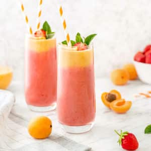 smoothie made of strawberries and apricots in glasses with apricots and strawberries sprinkled around.