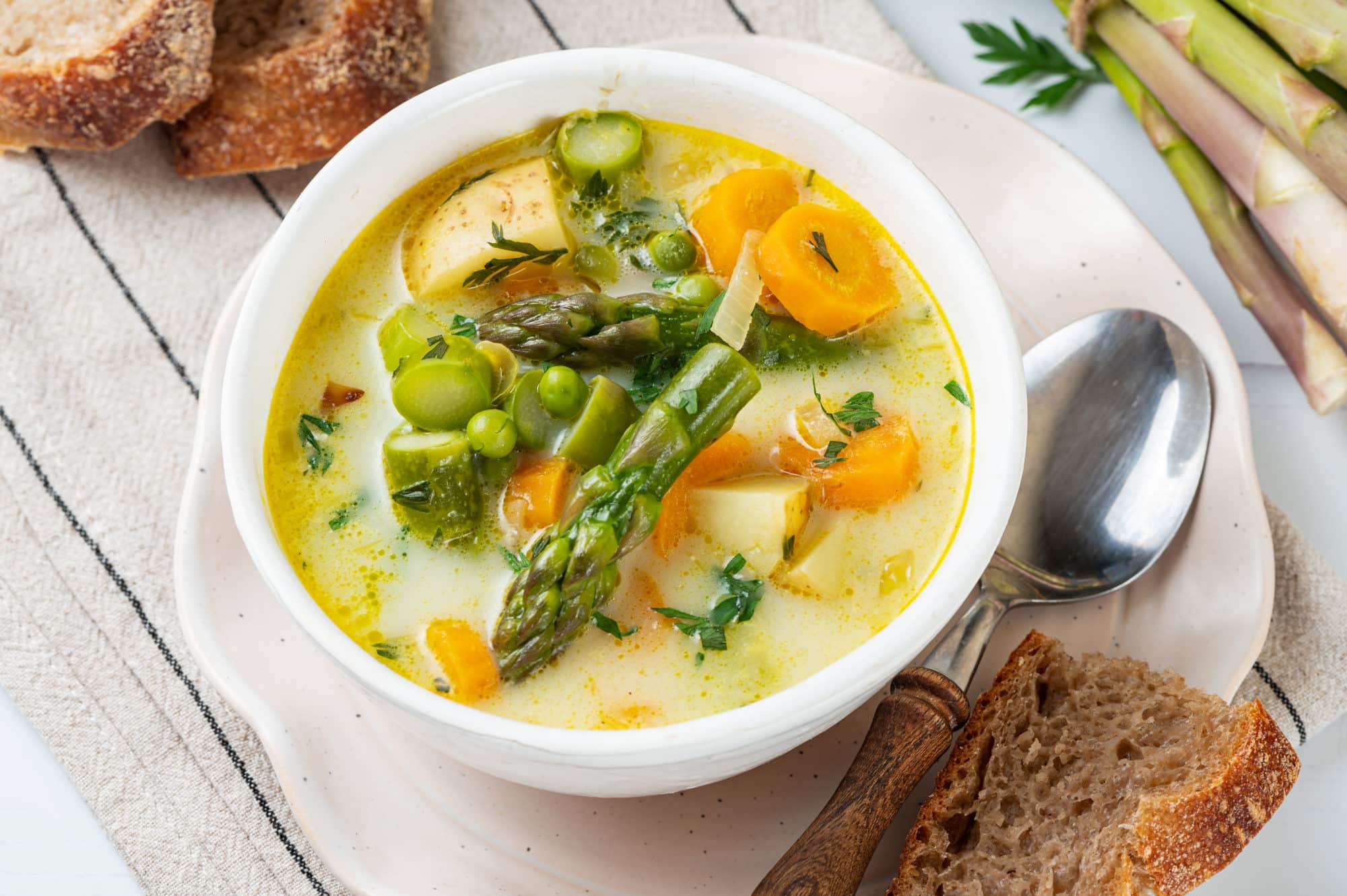 asparagus soup in a white bowl topped off with asparagus and carrot pieces.