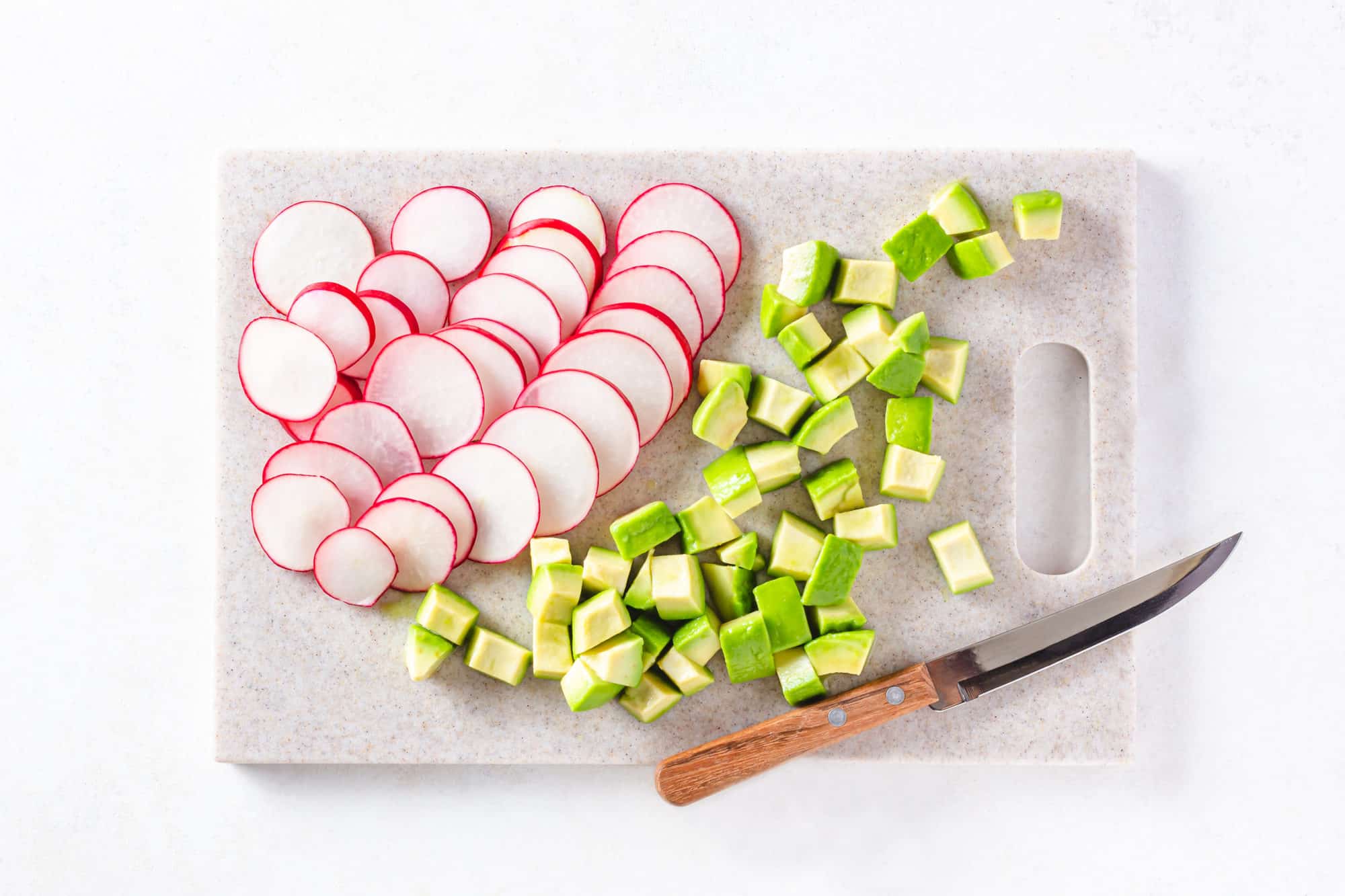 Chopped avocado and radishes on a cutting board with a knife on the side.