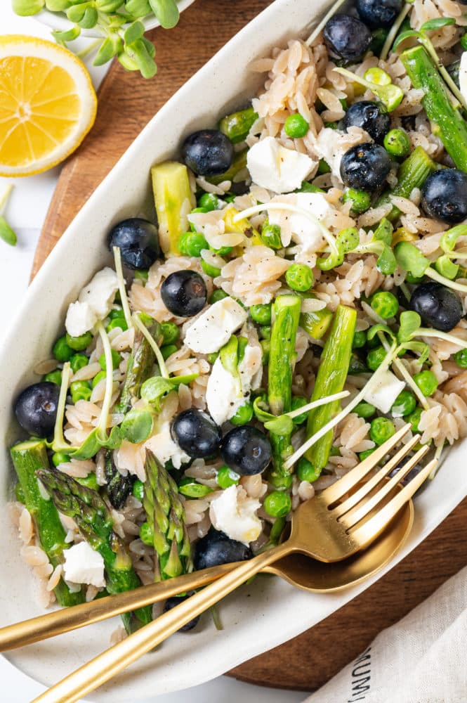 blueberries atop a lemon orzo salad with silverware on the side and a lemon wedge.