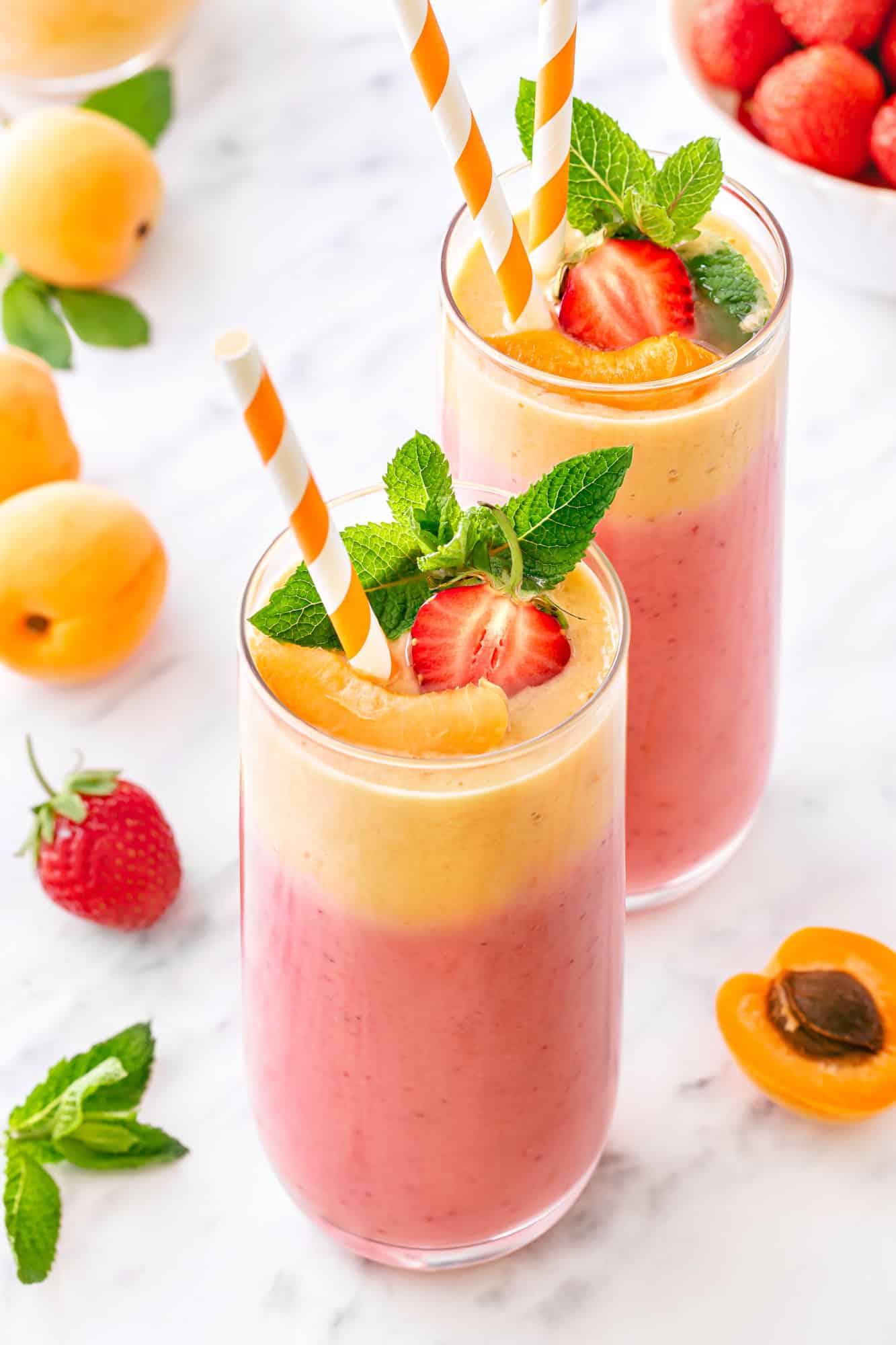 Apricot smoothie in a tall clear glass with a striped straw and a strawberry 