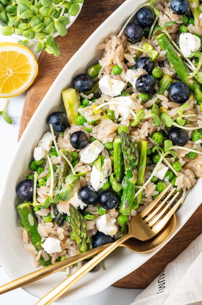 lemon-orzo-salad-in-a-plate-with-gold-fork-and-spoon-on-a-wooden-board