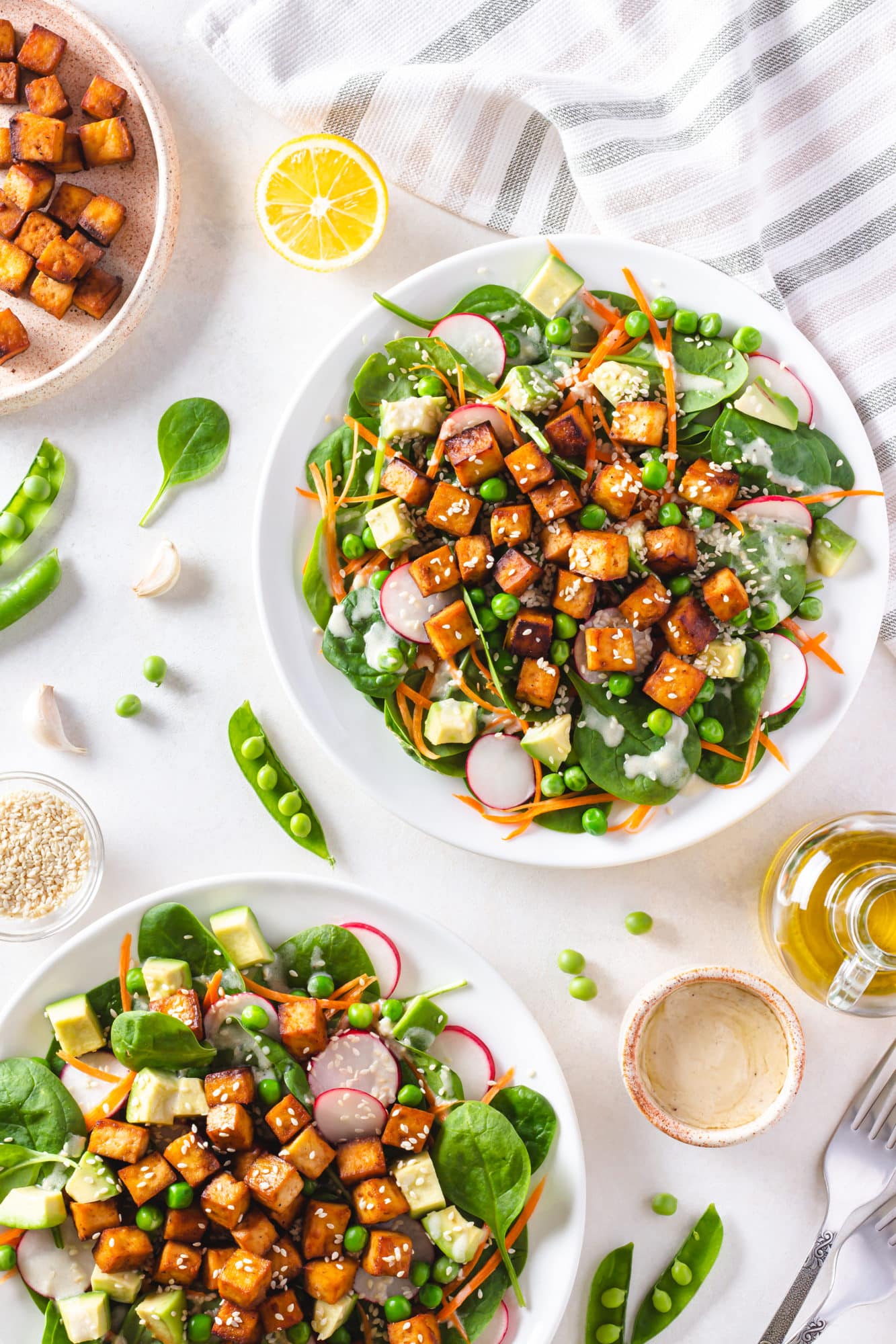 tofu salad on two white plates with peas olive oil and other ingredients scattered around