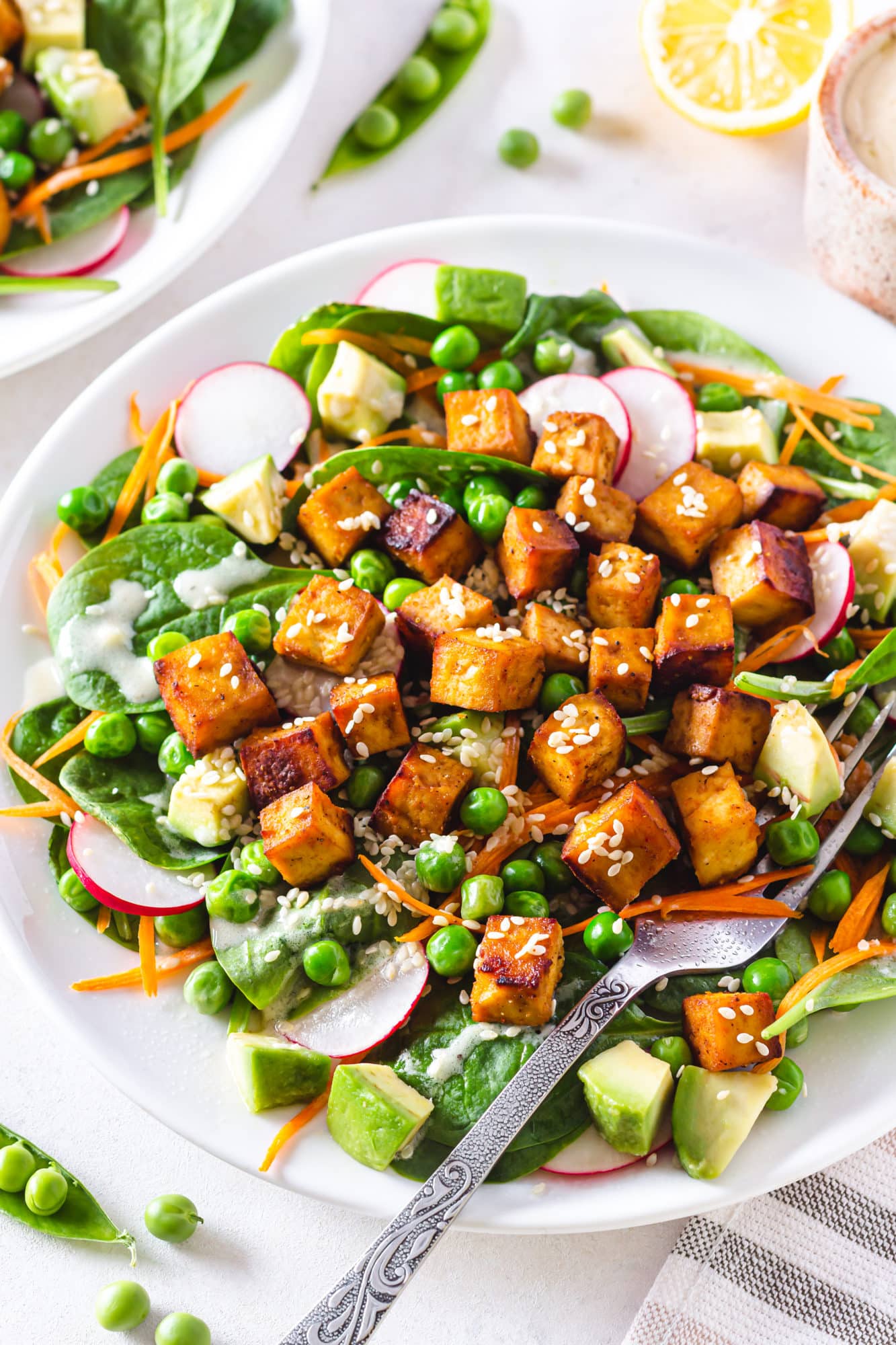 a white plate with crispy tofu salad on it with a silver fork on the side.