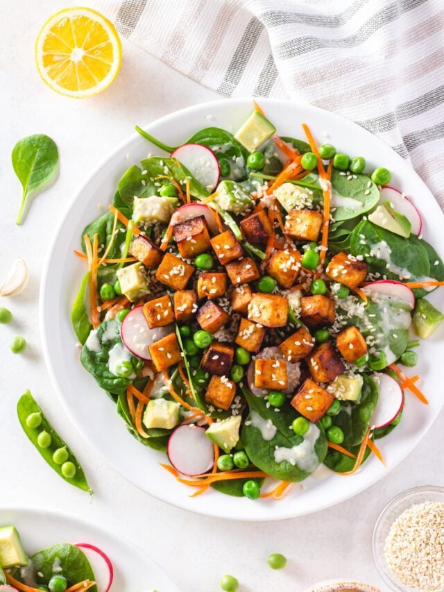 Tofu salad on a white plate with a striped towel and a lemon wedge.