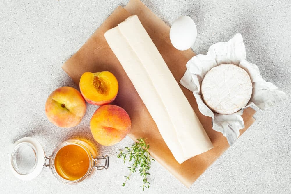 prepared ingredients for peach and brie tarts puff pastry brie thyme peaches egg and honey.