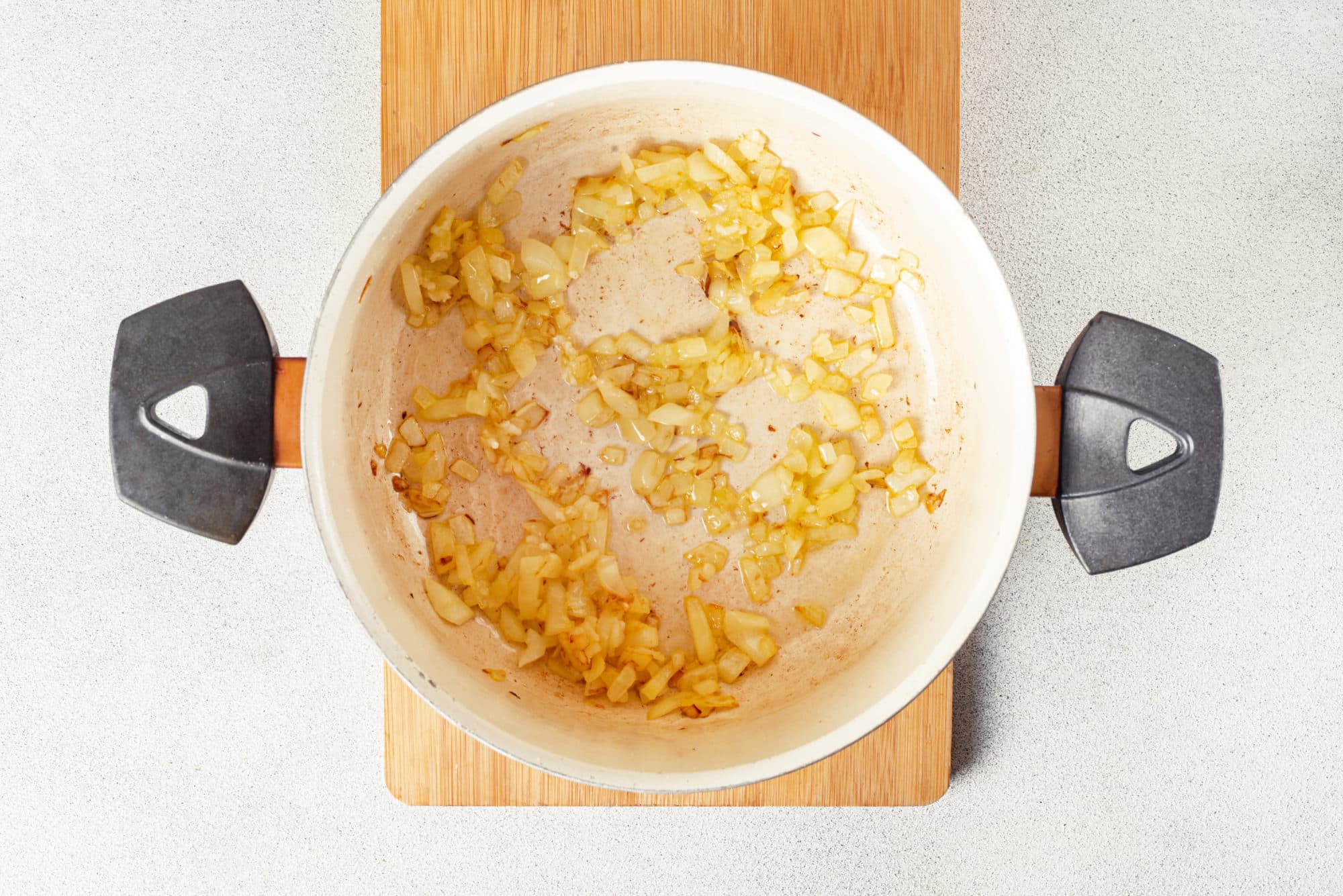 onion sauteing in a pot on a wooden board.