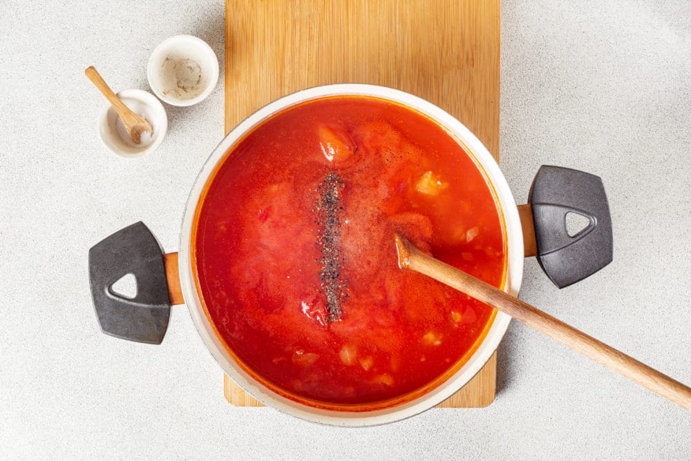 process of cooking tomato soup in a pot on a wooden board with spices added on top.