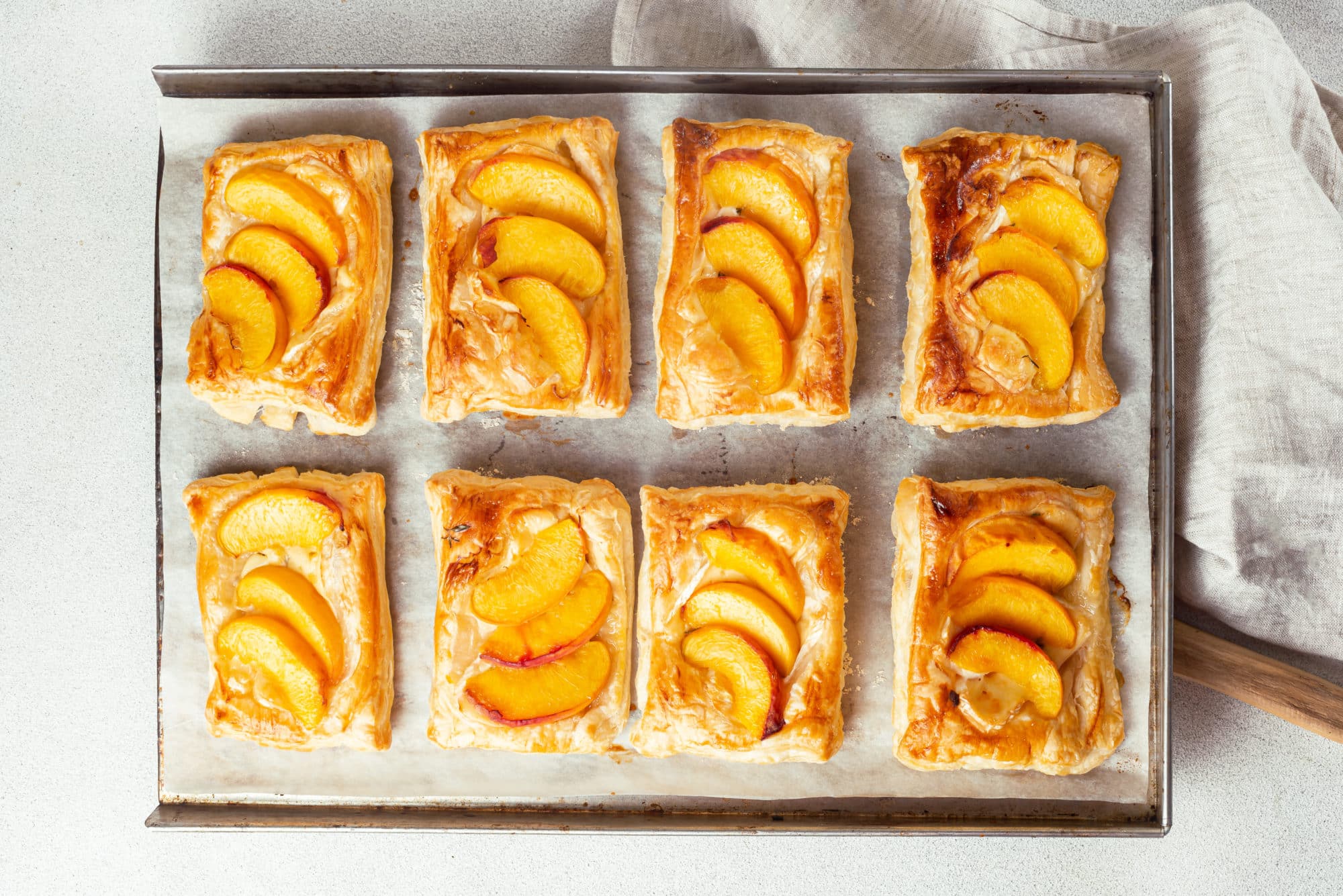 a baking tray with baked brie and peach tarts on it.