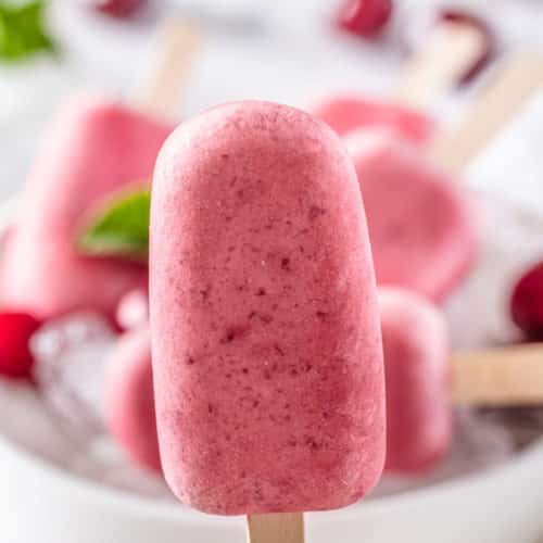 cherry ice pops on a wooden stick with a bowl of ice in the background.