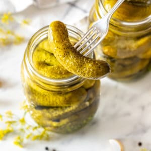 a jar of pickles with one pickle speared with a fork.