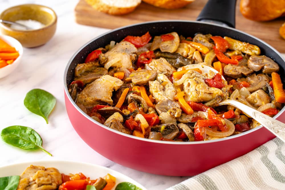 a pan with chicken thighs olive oil sliced carrots cherry tomatoes and basil leaves in it.