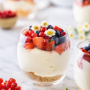 a glass filled with an individual cup of cheesecake with berries on top.