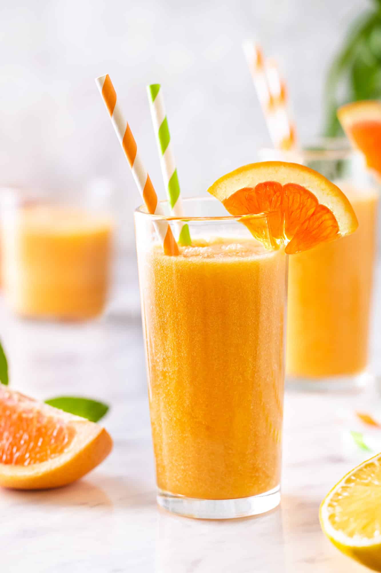 Citrus smoothie in a glass with an orange wedge on the rim and two straws.