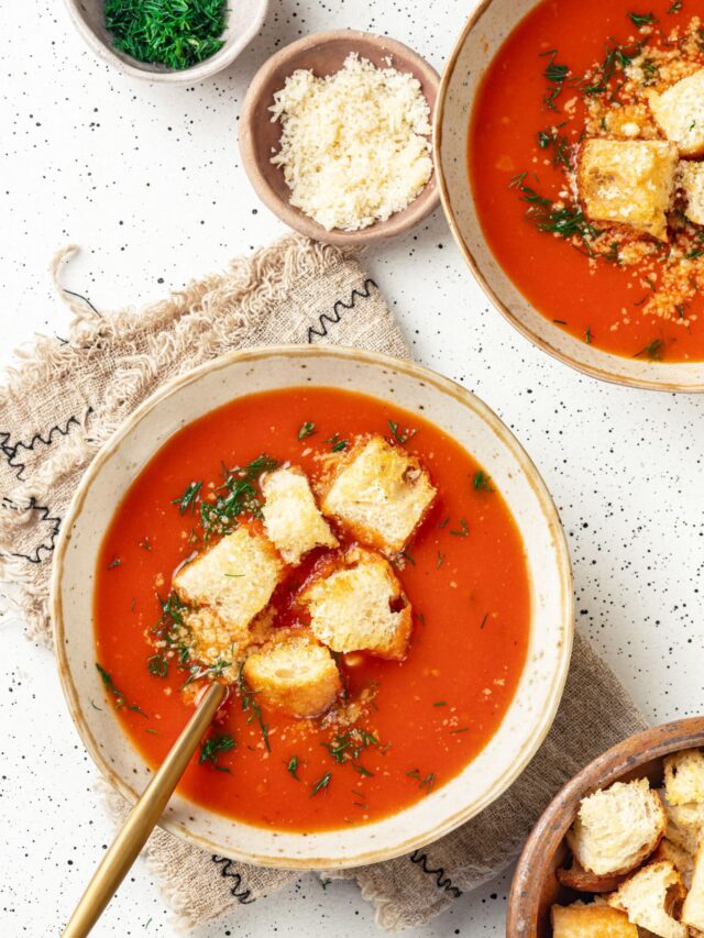 tomato soup with croutons on top of a bowl with a spoon on a towel.