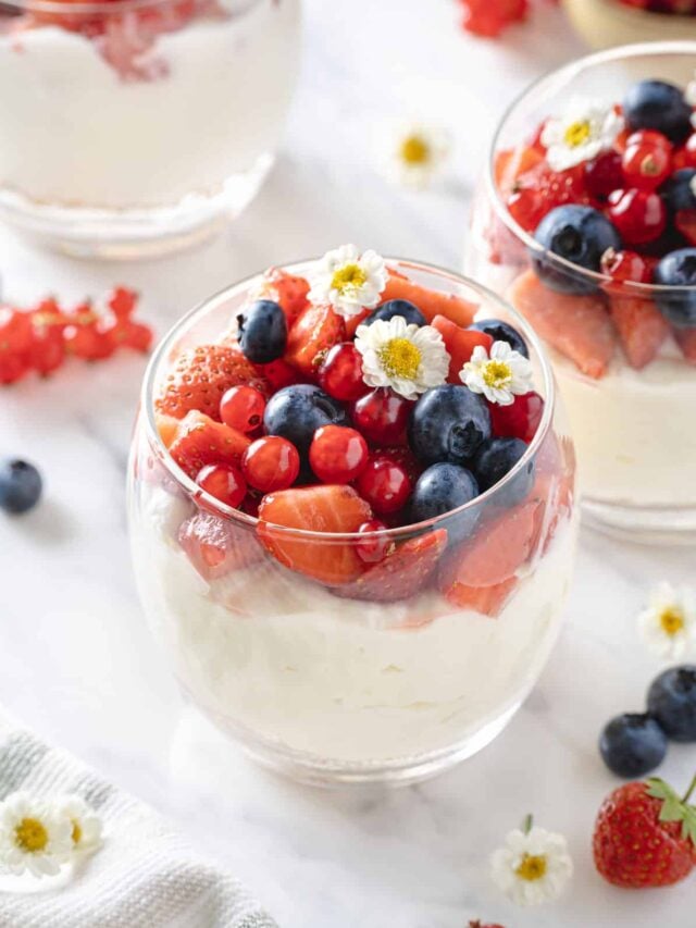 cheesecakes with berries and daisies on top in glass cups with more berries on the side.