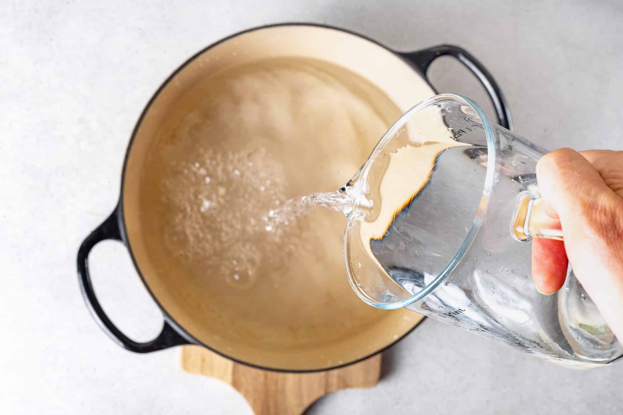 water-being-added-to-a-soup-pot-from-a-glass-pitcher-on-a-wooden-board
