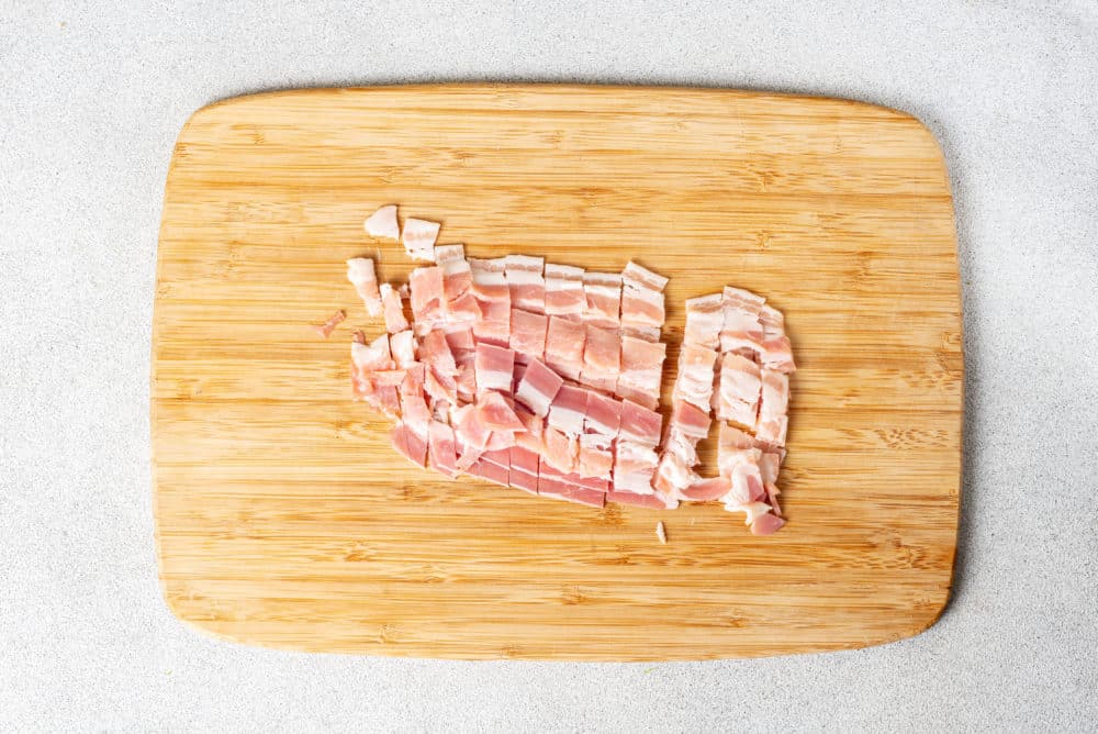 a wooden cutting board with chopped bacon on it.