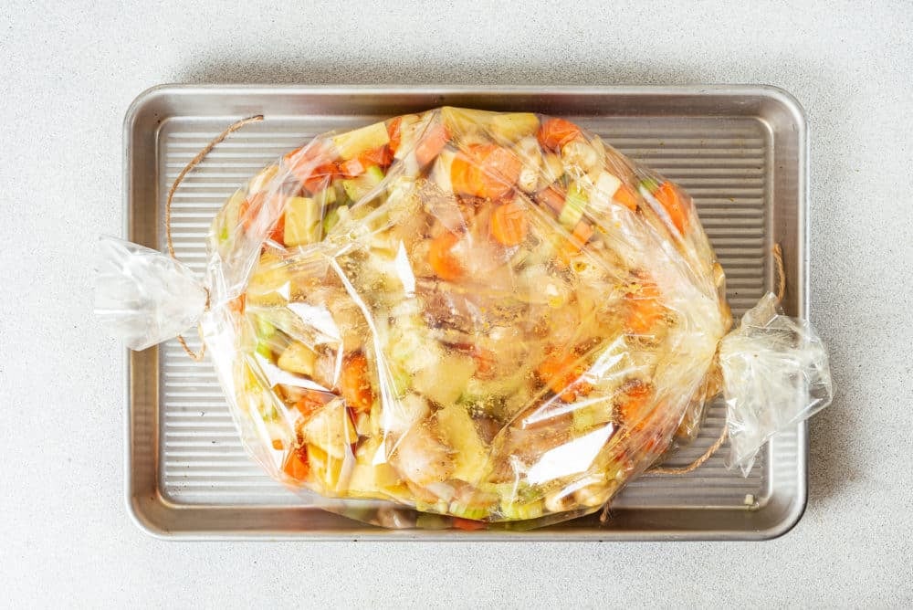 raw chicken and veggies in an oven bag on a baking sheet.