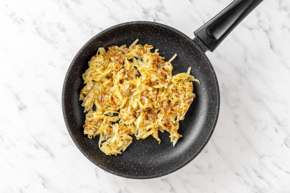hash browns cooking in a black pan.