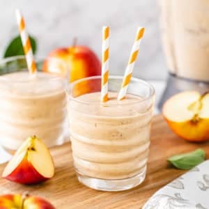 apple-smoothie-in-a-clear-glass-with-straws-on-a-wooden-board
