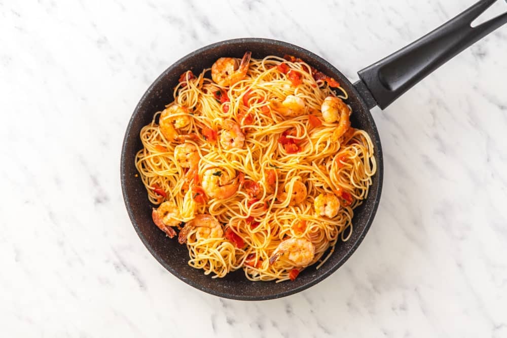pasta shrimp and tomatoes combined in a black pan.