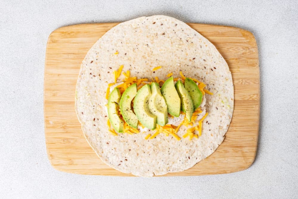 a tortilla with chicken, avocado and cheese on a wooden cutting board
