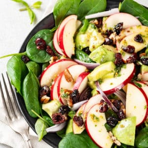 spinach avocado apples red onion dried fruits and walnuts in a salad.