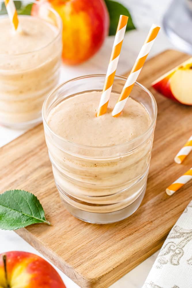 apple-smoothie-in-a-clear-glass-with-two-straws-on-a-wooden-board