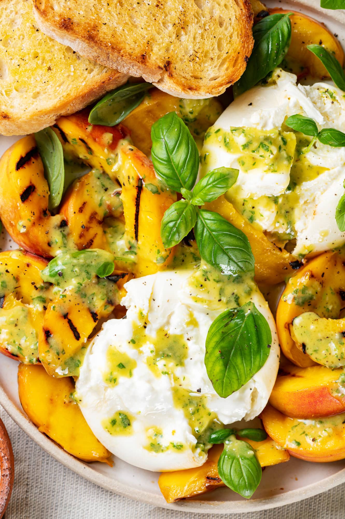 a white plate with burrata and grilled peaches salad with drizzled dressing and basil leaves on top.