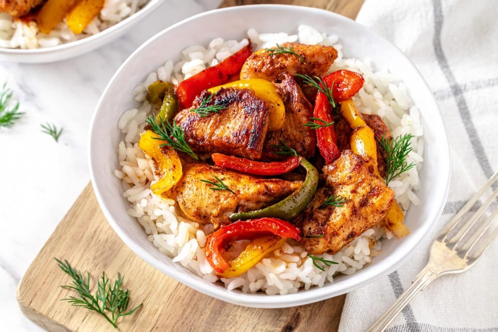 chicken-and-bell-peppers-with-rice-in-a-white-bowl-with-a-fork-on-the-side-on-a-wooden-board-with-a-white-towel
