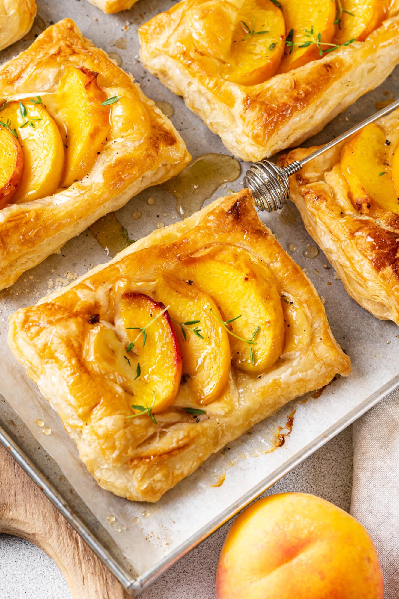 Peach brie tarts on a baking tray topped with a sprinkle of thyme and a drizzle of honey.