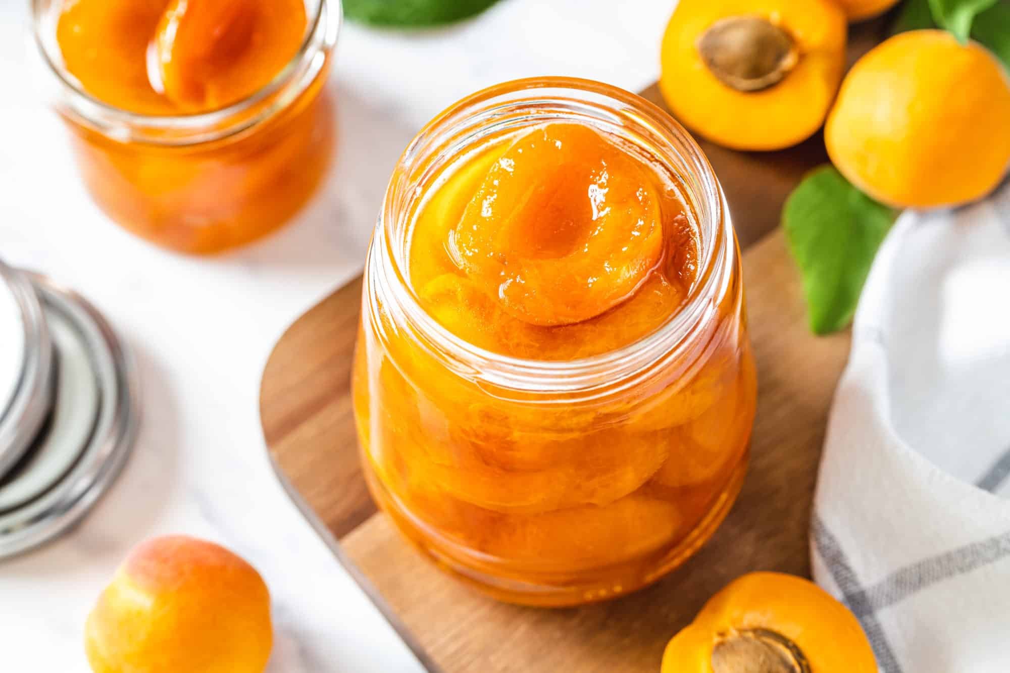 Apricot jam in a glass jar on a wooden board.