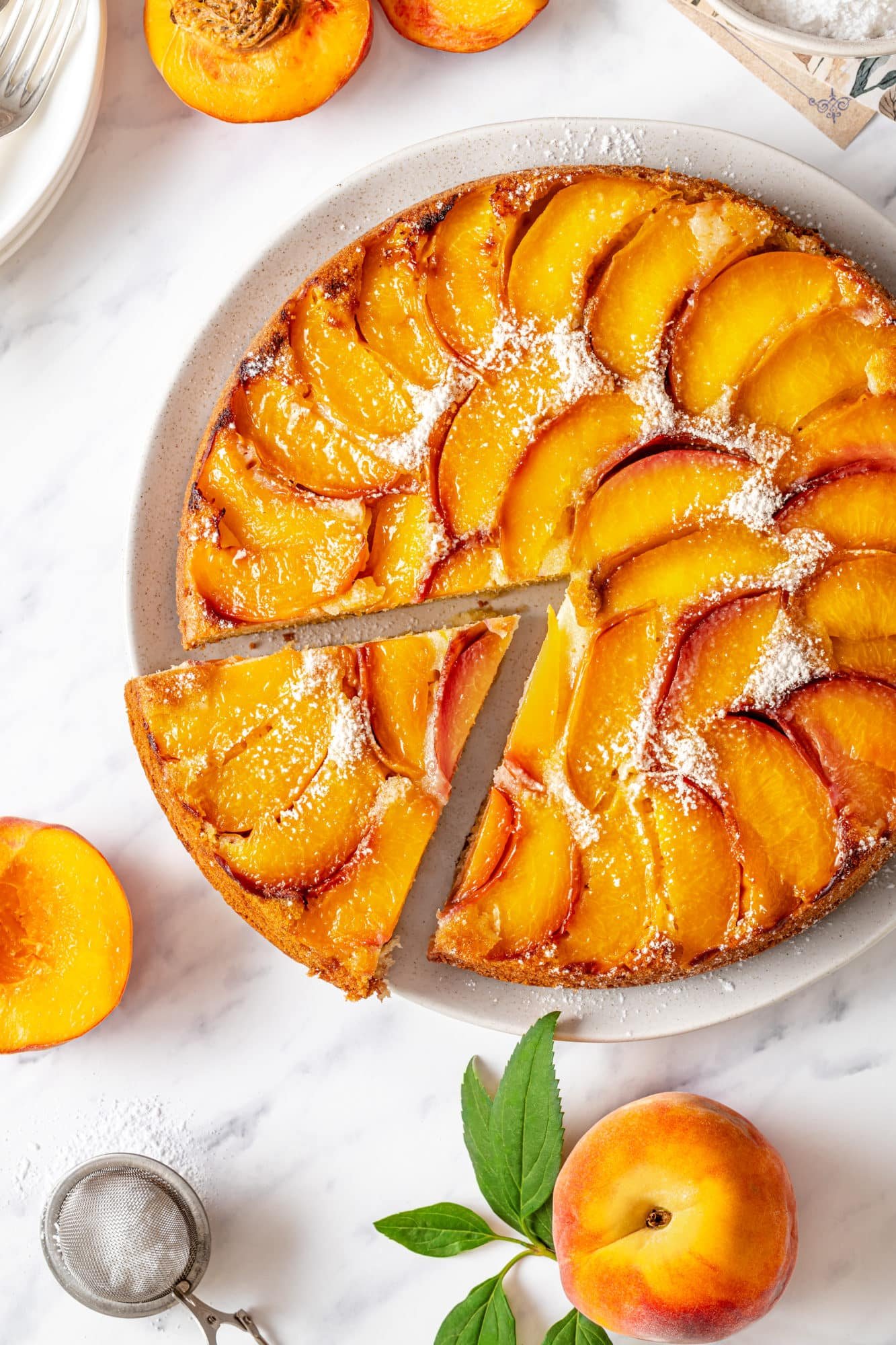 Slice of peach upside down cake on a white plate with the rest of the cake.