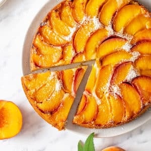 Slice of peach upside down cake on a white plate with the rest of the cake.