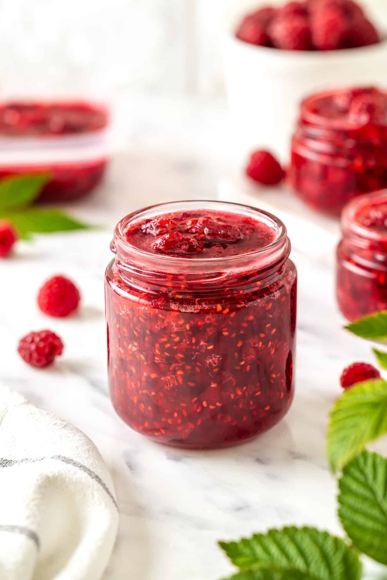 raspberry-jam-in-a-clear-jar-with-raspberries-around-and-more-jars-of-jam-in-the-background