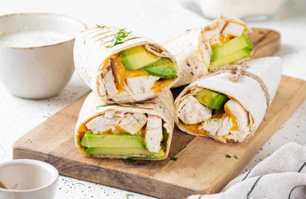 a small stack of grilled chicken and avocado wraps on a cutting board
