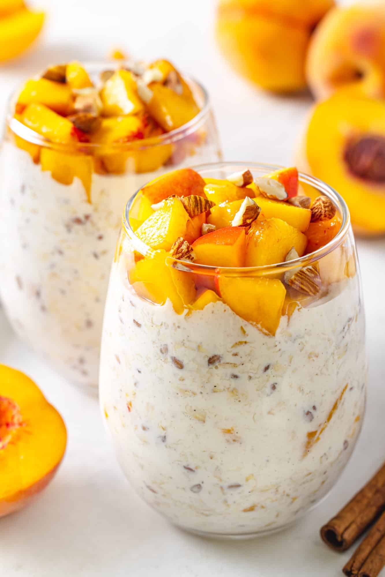 peach overnight oats on a marble board with whole peaches and cinnamon sticks seen in the background
