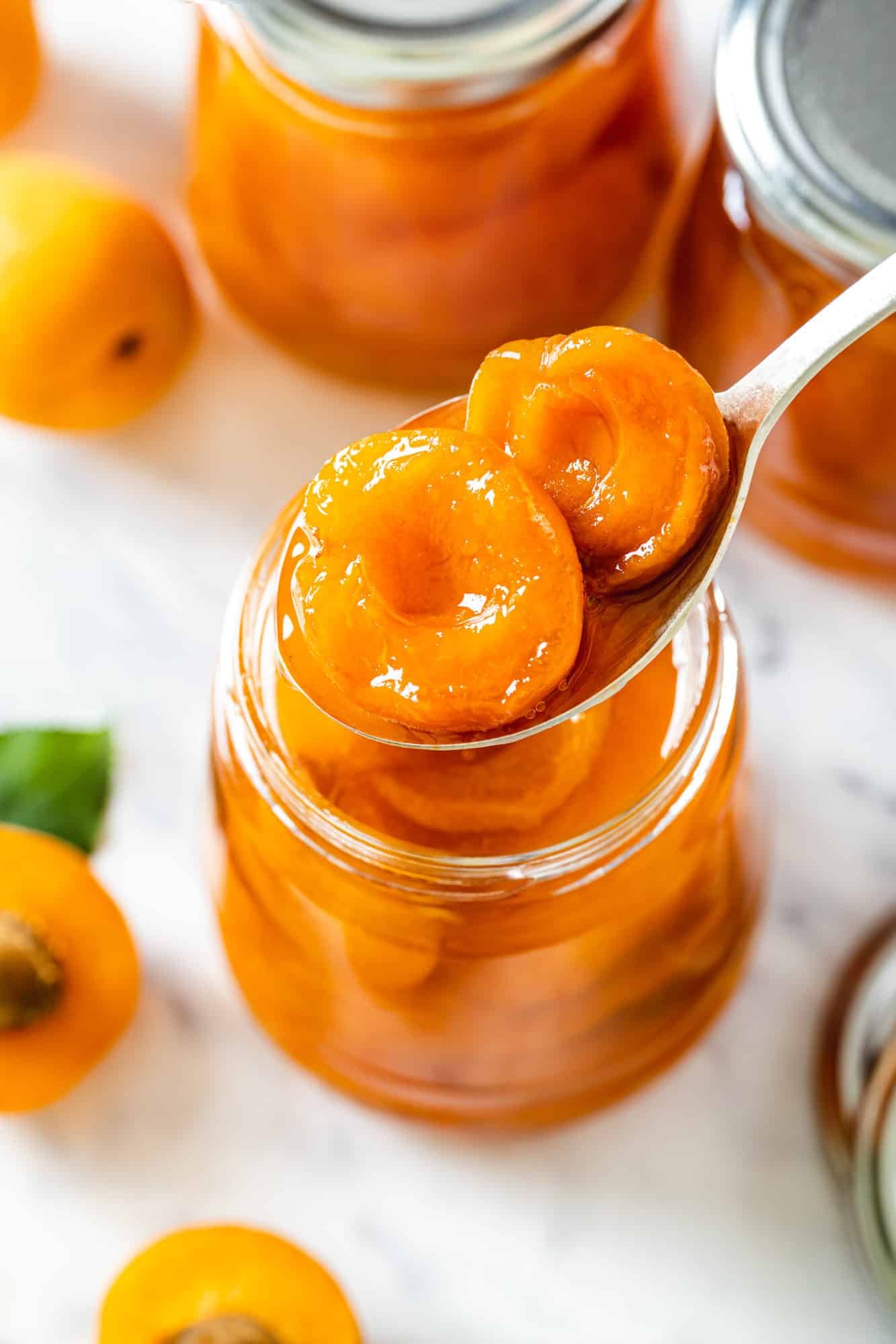 a spoon over a glass jar filled with apricot jam.