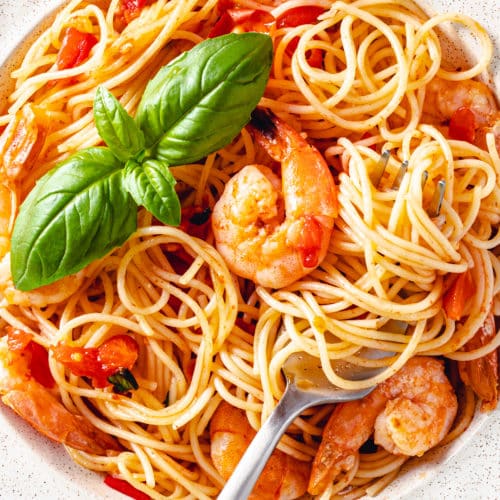 a white bowl filled with shrimp tomato pasta with basil on top and a fork.