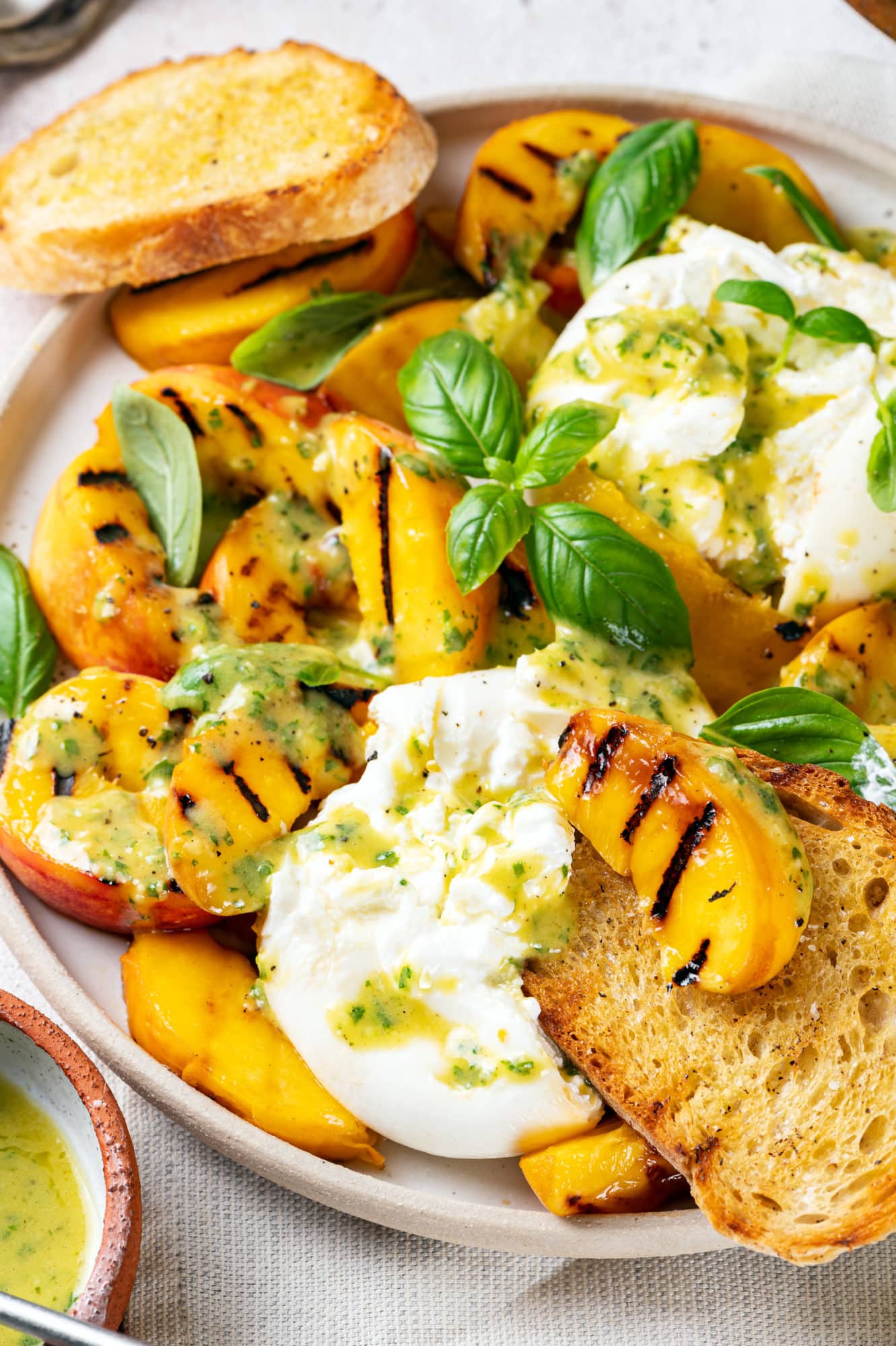 close up of peach burrata salad with bread slices and with basil on top.